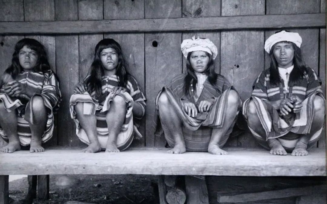 Four indigenous persons seated against a wooden wall.