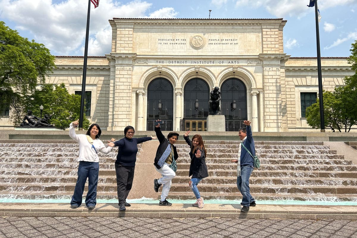 Five people posing with arms outstretched in front of a museum