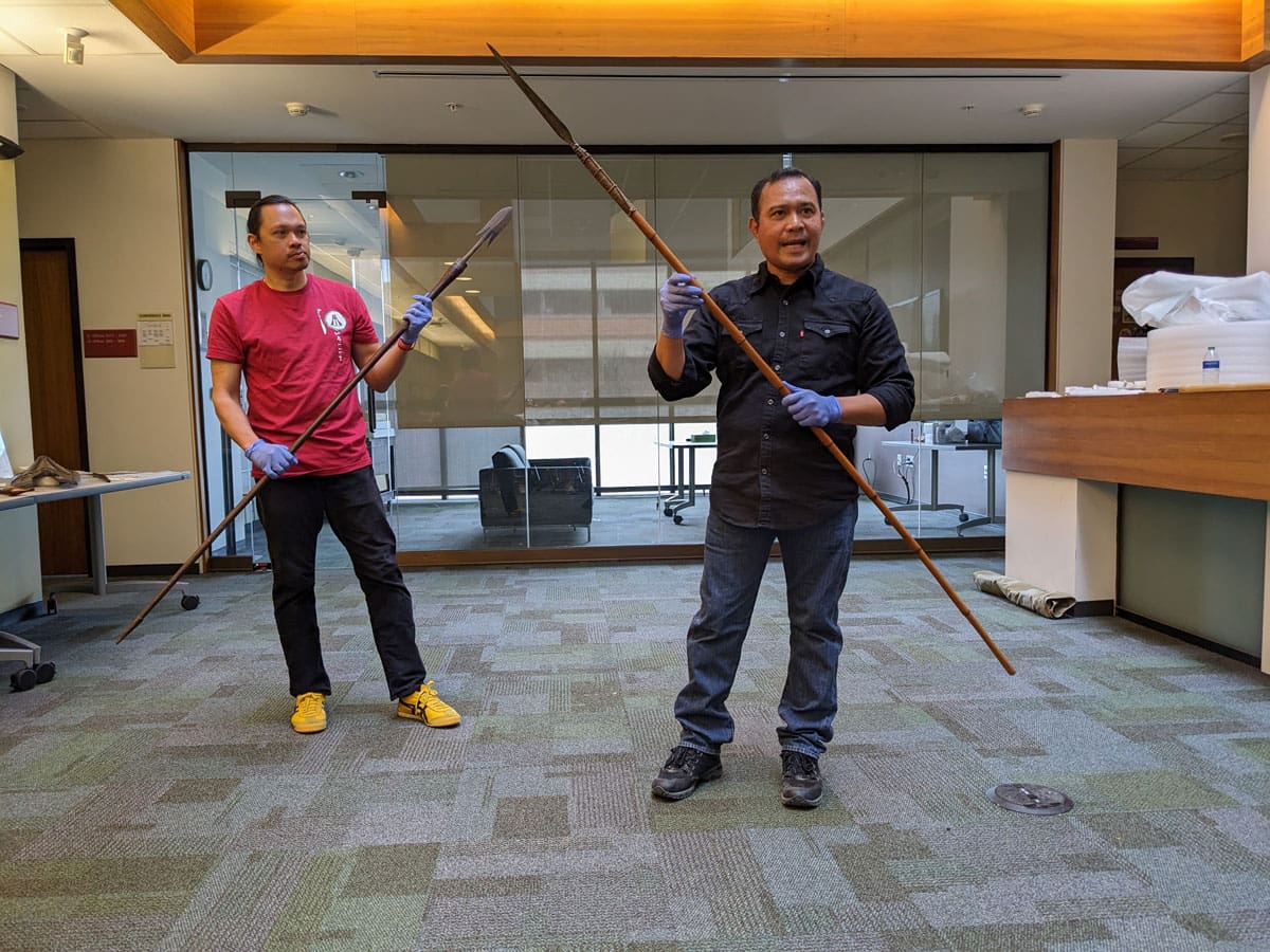 Two men demonstrating how to handle spears in a workshop.