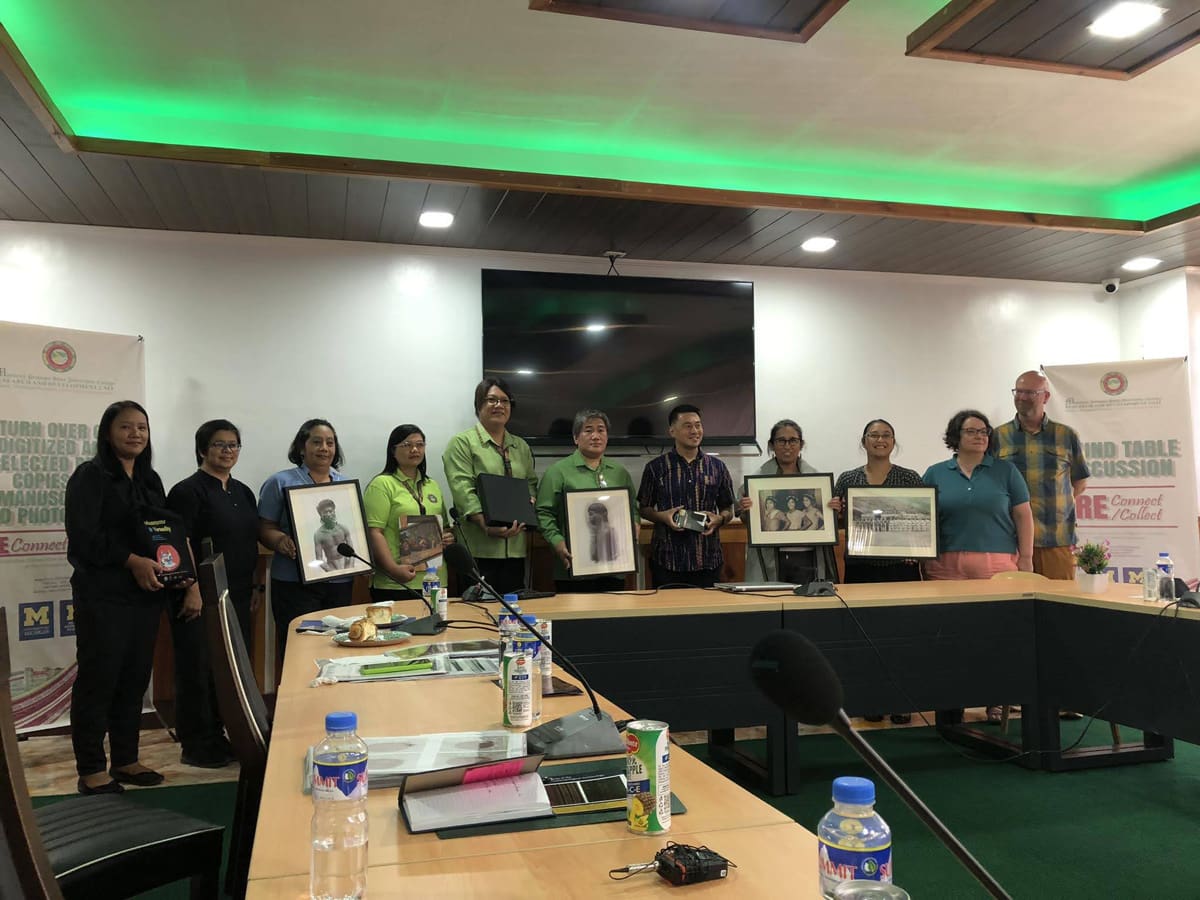 A group of people holding photos around a conference table.