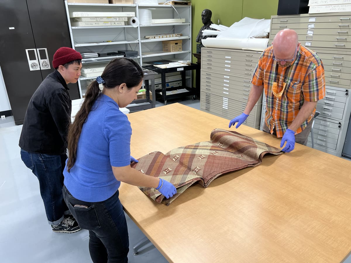 Three people unfolding a large woven mat.