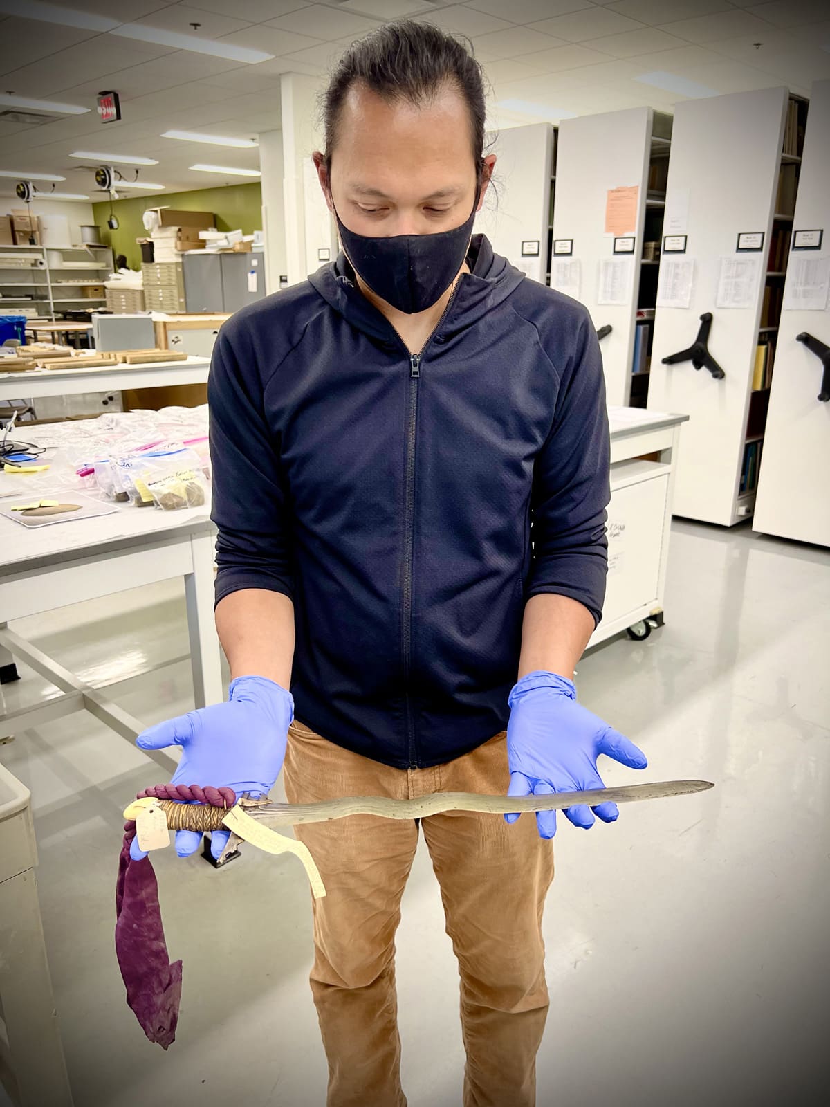 A man with blue protective gloves holding a long dagger.