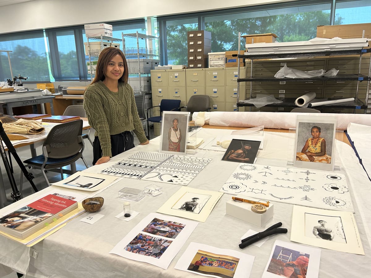 A woman standing next to a table exhibiting various tattoo patterns.