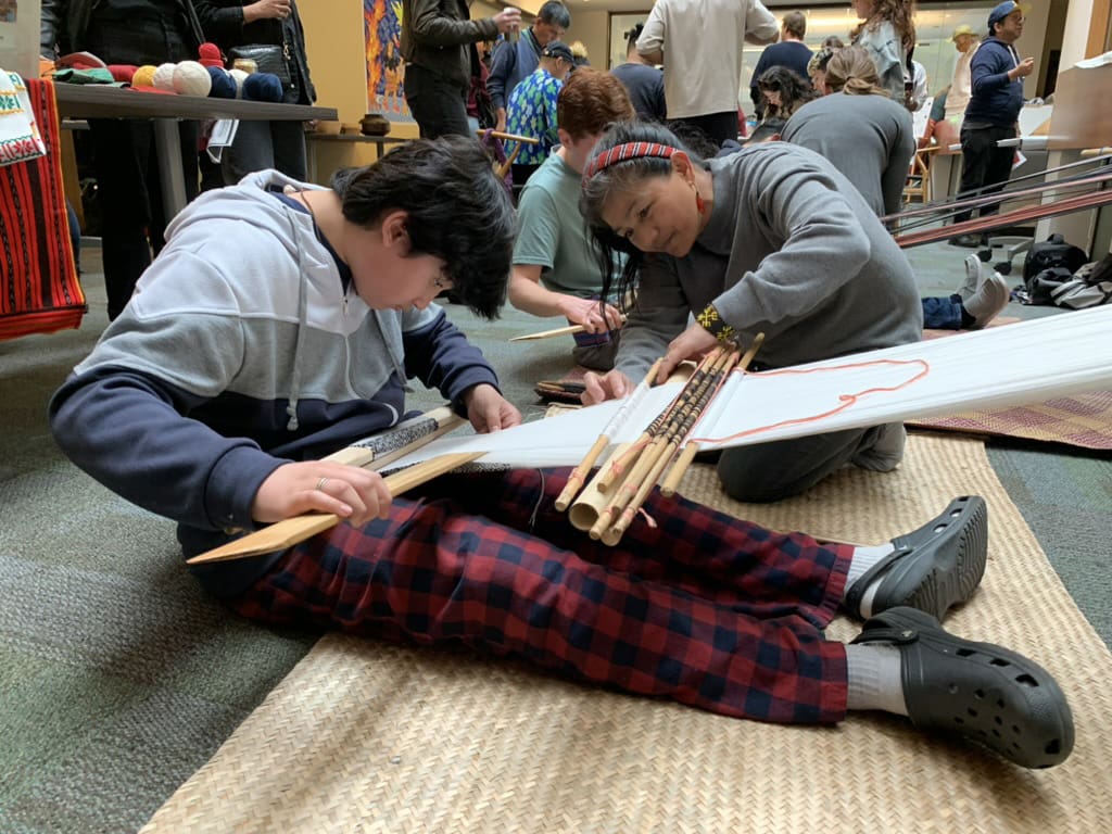 A woman shows a boy how to weave.